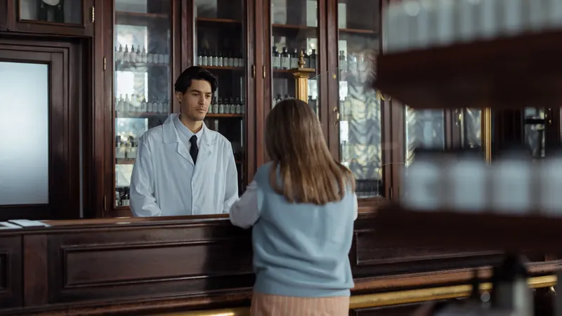 A woman seen from behind at a pharmacy counter, waiting to be served.